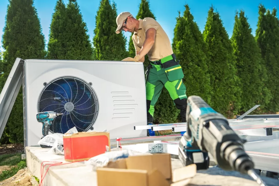 HVAC technician on roof installing heat pump with tools in foreground.